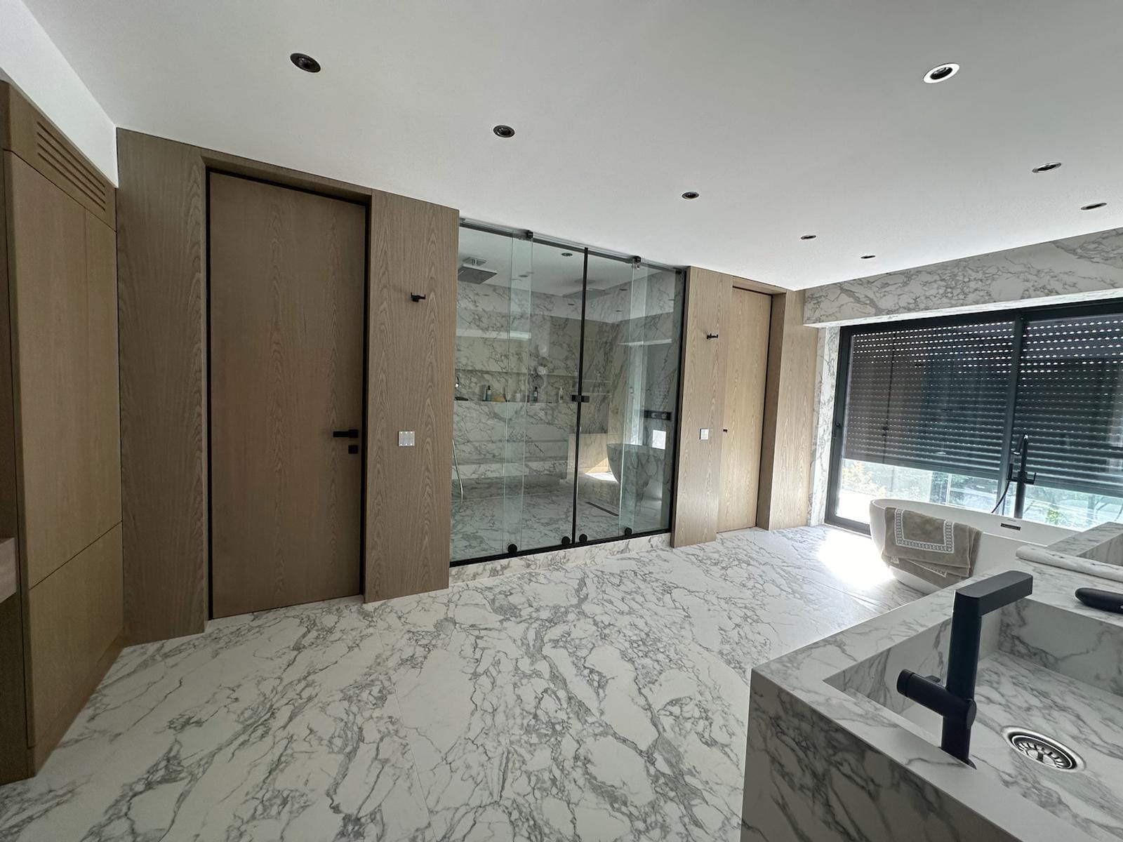 Ahşap yüzeyler ve cam duş bölümüyle birlikte görülen damarlı porselen banyo zemini ve lavabo detayı